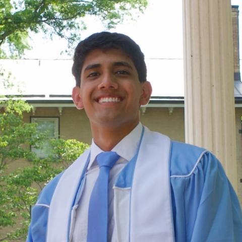 headshot of Dev smiling in blue graduation gown and tie